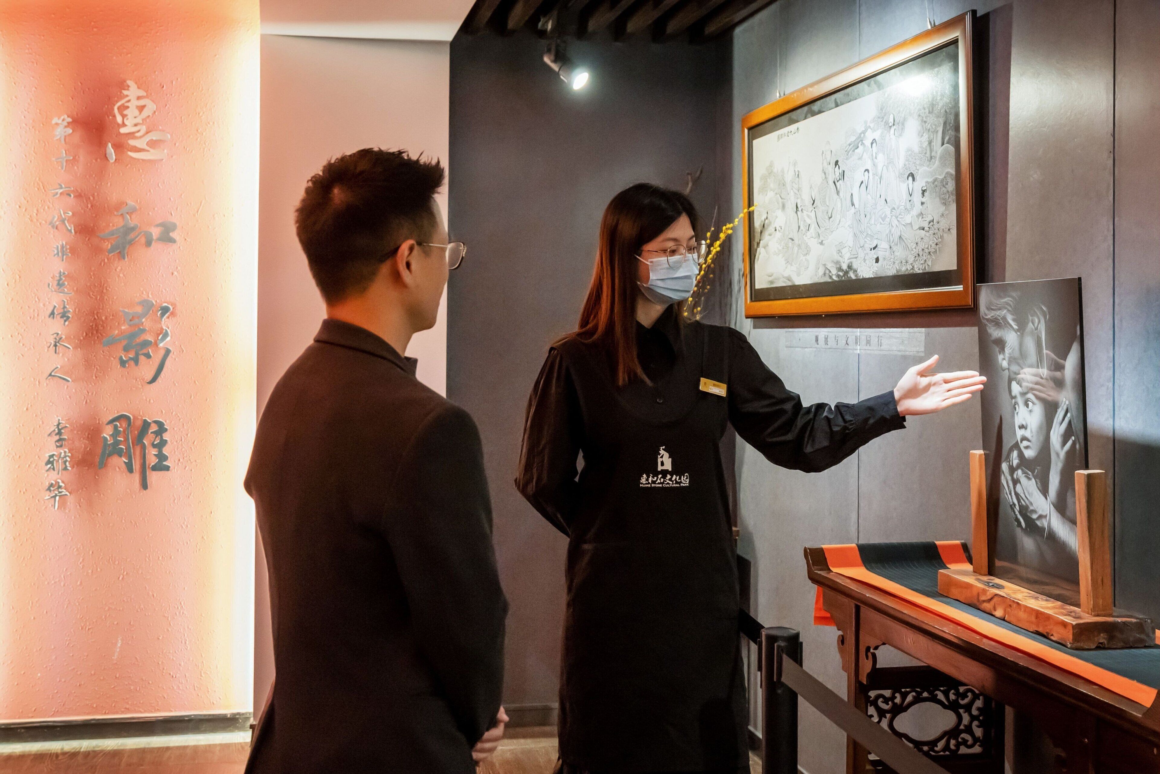 Eine Person in Uniform, schwarz, steht neben einem Tisch mit einem gerahmten Kunstwerk und einer Präsentationsvitrine.