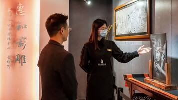 Eine Person in Uniform, schwarz, steht neben einem Tisch mit einem gerahmten Kunstwerk und einer Präsentationsvitrine.
