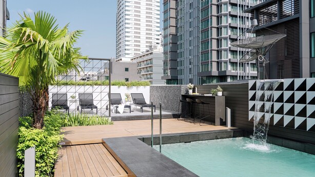 A rooftop pool area with a waterfall feature, lounge chairs, and a bar area.