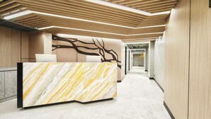 A modern reception area with a marble reception desk, wooden paneling, and a long hallway.