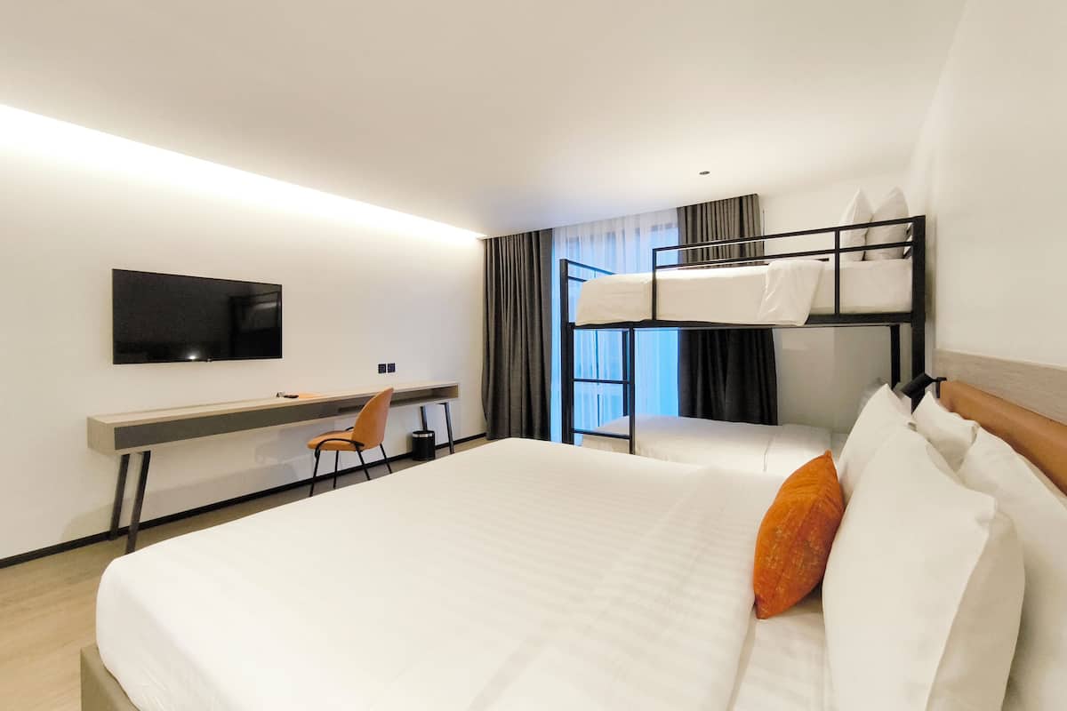 Ein Hotelzimmer mit Etagenbett, Schreibtisch mit Stuhl, Flachbildfernseher und einem Fenster mit Vorhängen.