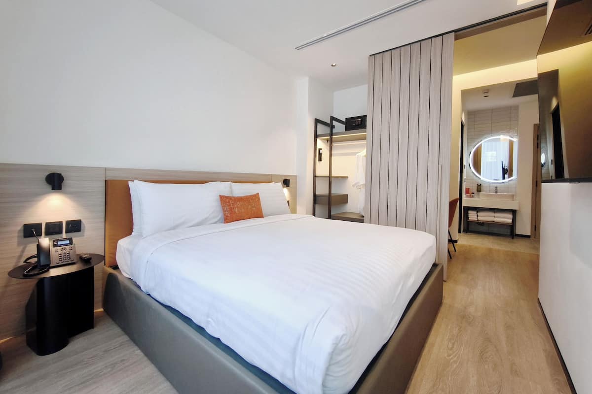 Ein modernes Hotelzimmer mit einem großen Bett, einem Nachttischtelefon, einem kleinen Tisch und einem begehbaren Kleiderschrank mit Spiegel.