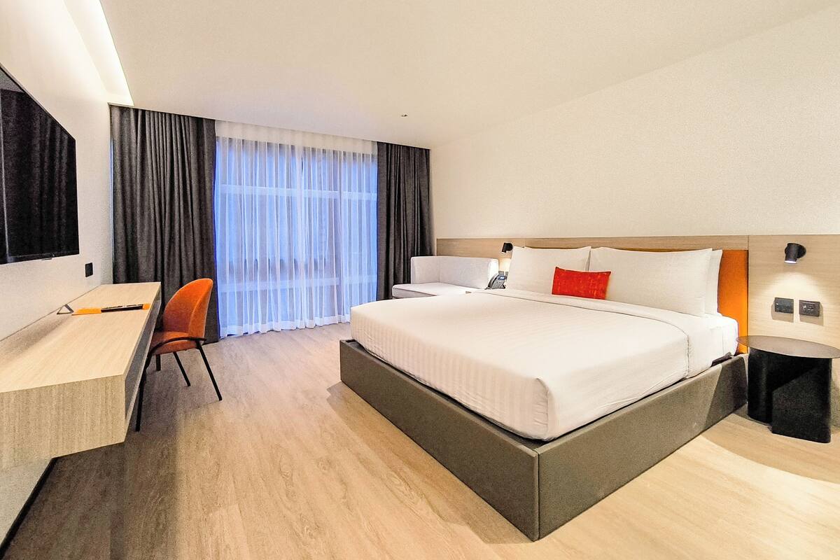 Ein Hotelzimmer mit einem großen Bett, einem Schreibtisch, einem Stuhl und einem Fernseher.