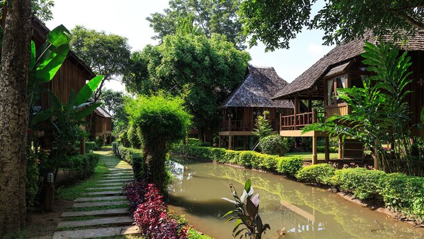 A serene garden with a water canal, wooden buildings, and lush greenery. - Belle Villa Resort Pai (Pai)