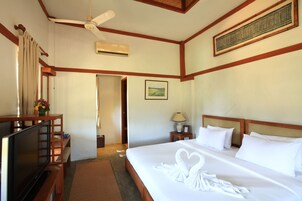 Habitación de hotel con cama, televisión, ventilador de techo y un cuadro en la pared.