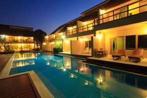 A swimming pool with lounge chairs and a deck area, surrounded by a building with multiple balconies and windows.