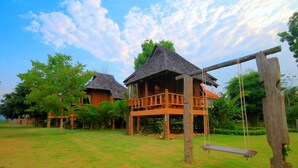 A wooden cabin with a balcony, surrounded by a grassy lawn and trees. - Belle Villa Resort Pai (Pai)
