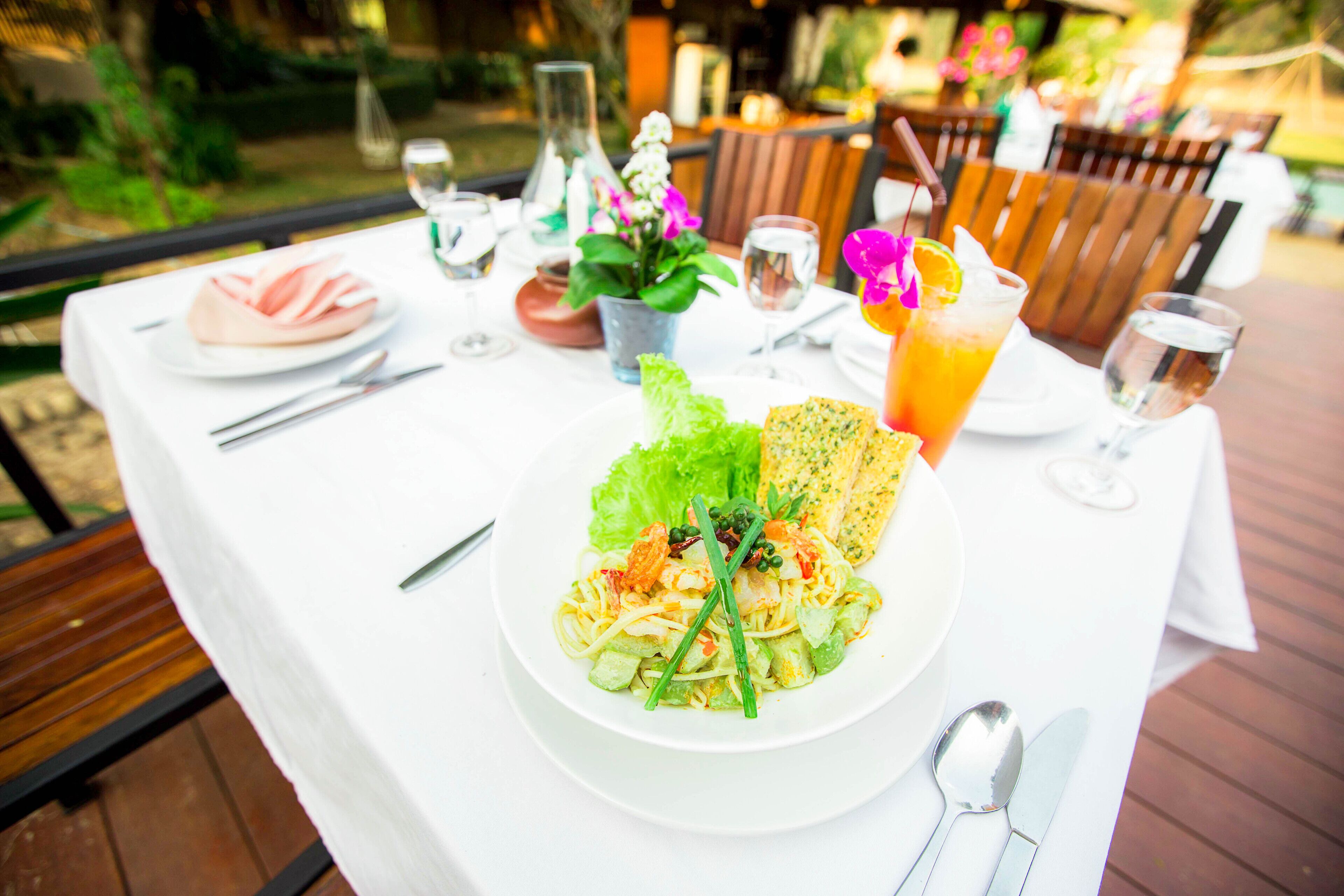 Una mesa de comedor al aire libre con un plato de comida, bebidas y cubiertos.