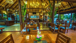 An indoor restaurant with wooden furniture, a bar area, and a view of the outdoors. - Belle Villa Resort Pai (Pai)