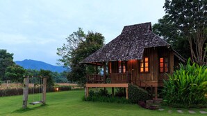 A wooden house with a thatched roof, a balcony, and a view of a mountain. - Belle Villa Resort Pai (Pai)