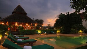 A poolside area with lounge chairs and a thatched-roof building. - Belle Villa Resort Pai (Pai)