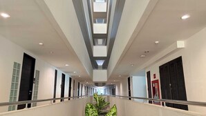 Un pasillo moderno de hotel con una escalera central, iluminación empotrada y una planta grande en maceta.
