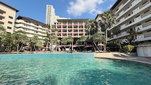 Un hotel con piscina, varios pisos, balcones y palmeras.