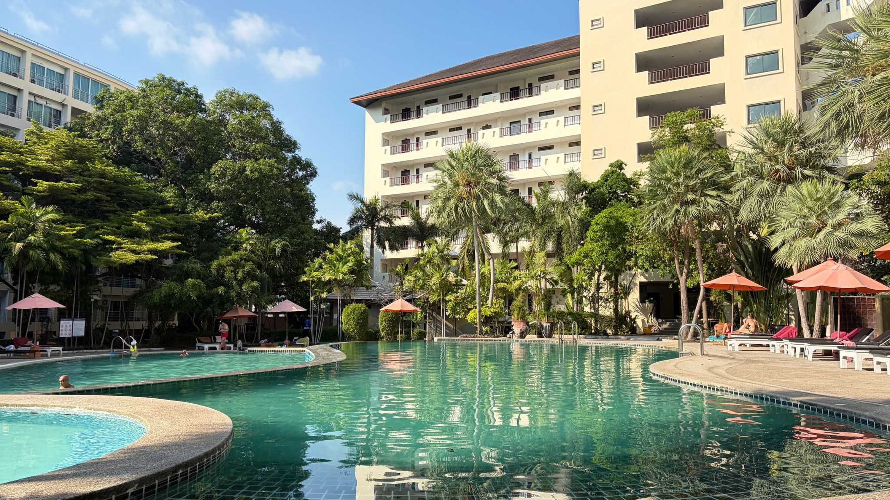 Ein Hotel mit großem Pool, umgeben von Palmen und Liegestühlen.