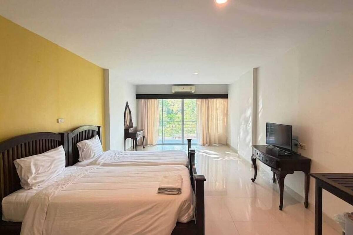 Quarto de hotel com duas camas, televisão, escrivaninha e vista para o exterior.