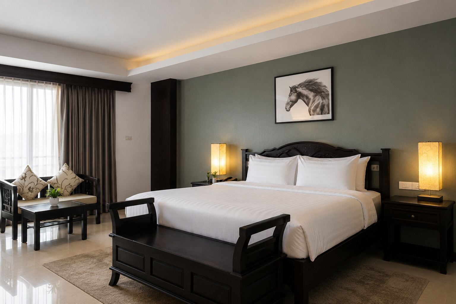A hotel room with a large bed, two bedside tables with lamps, a chair, a sofa with cushions, and a framed picture on the wall.