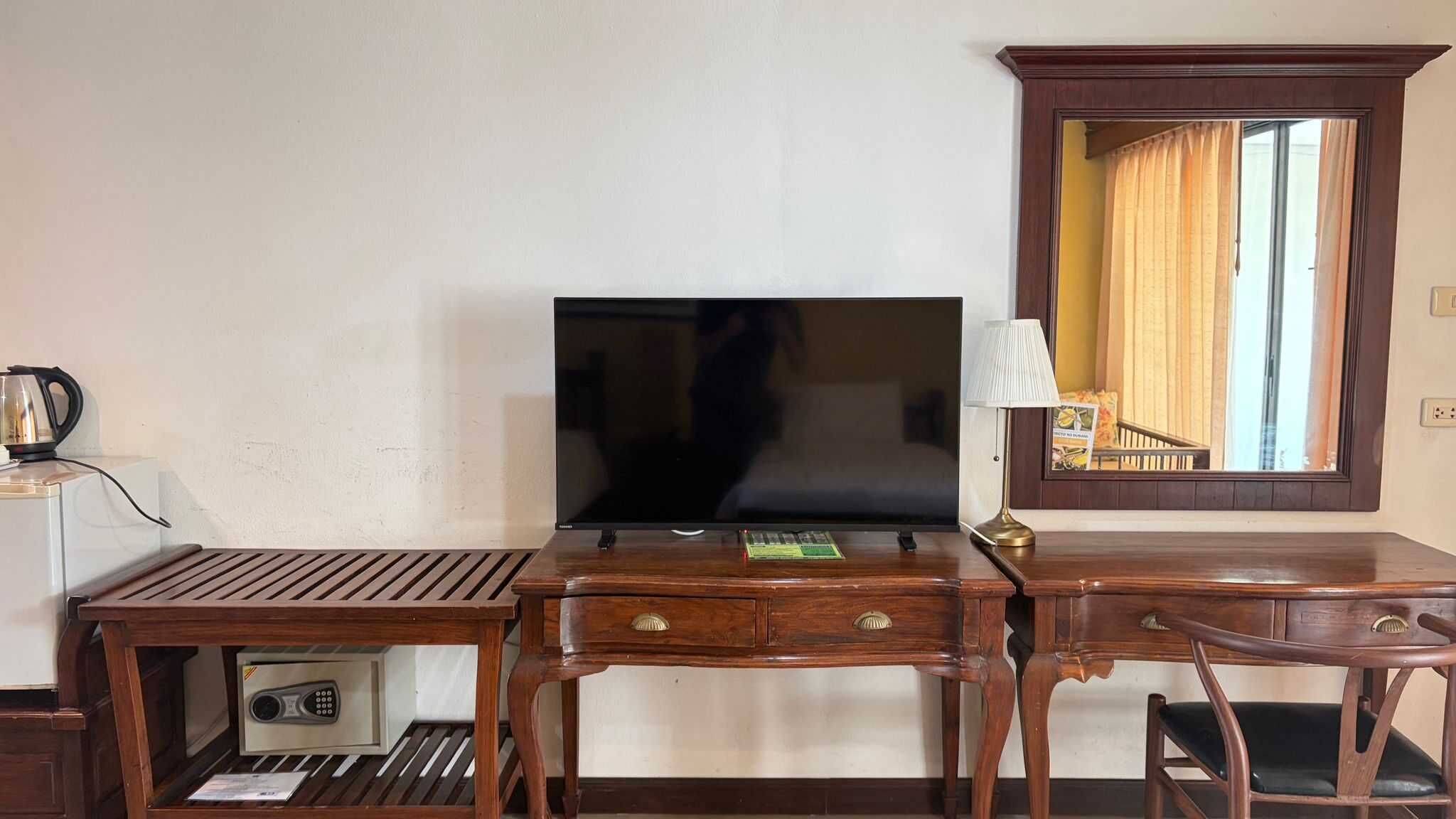 Habitación de hotel con escritorio de madera, televisor, espejo y ventana con cortinas.
