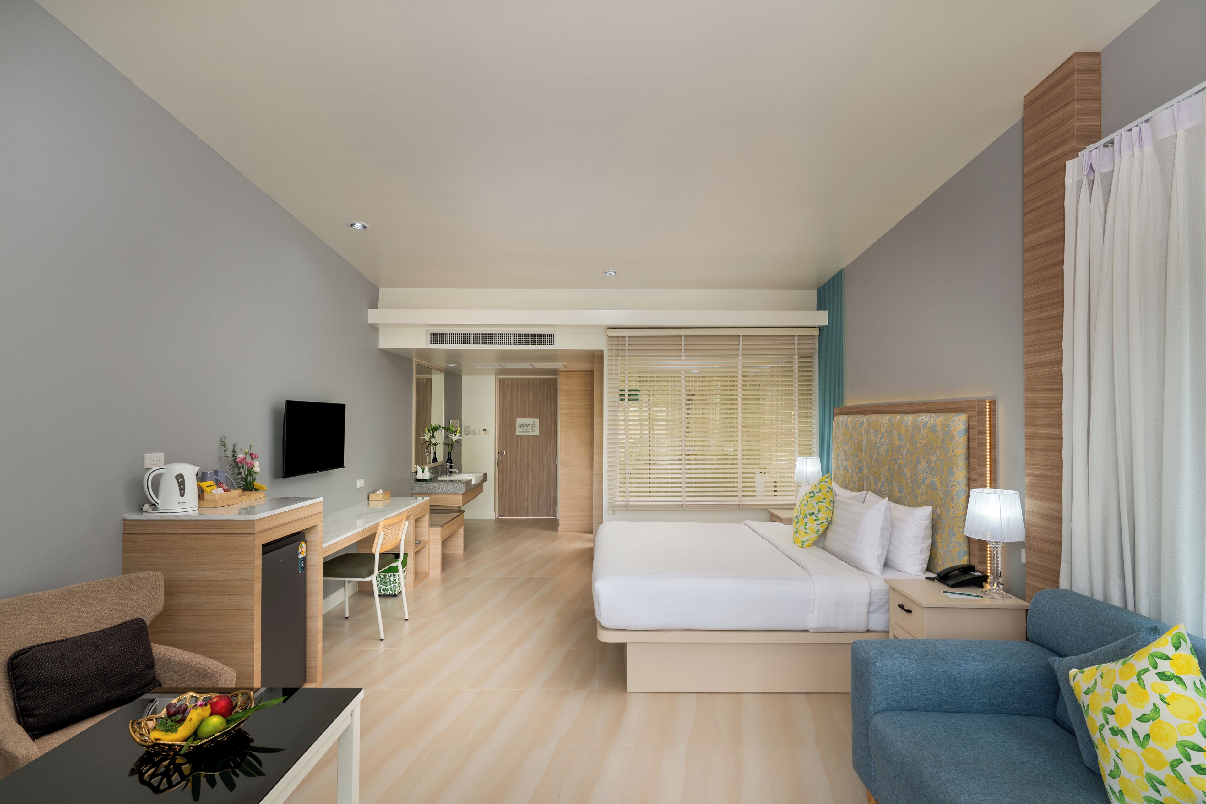 A hotel room with a bed, a desk, a chair, a sofa, and a TV.