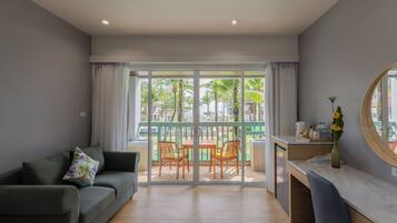 A modern living room with a sofa, a dining table with chairs, and a balcony with a view of palm trees.