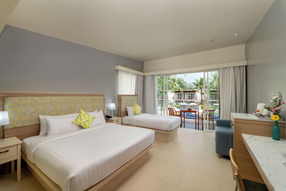 A hotel room with two beds, a desk, a chair, and a view of the pool and palm trees.
