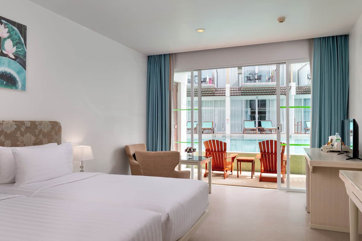 A hotel room with a bed, a desk, a chair, a table, and a view of a pool and outdoor seating area.