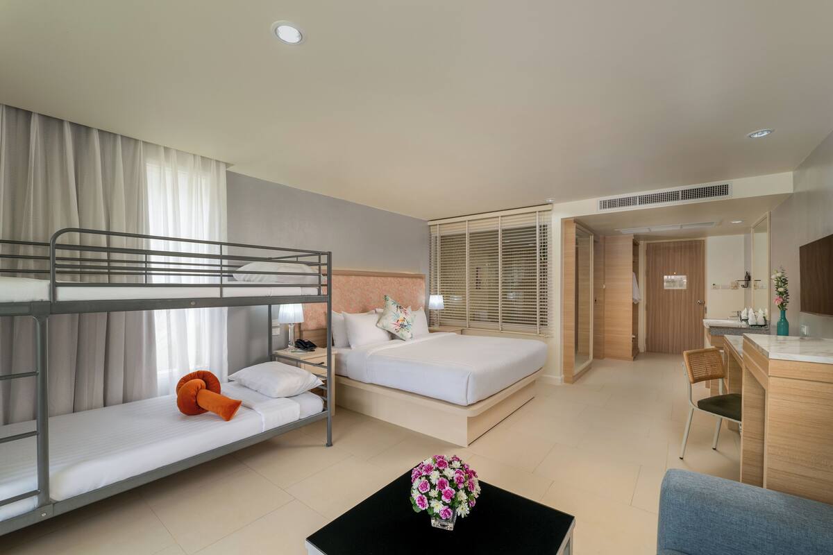 A hotel room with bunk beds, a desk, a chair, and a small table with a vase of flowers.