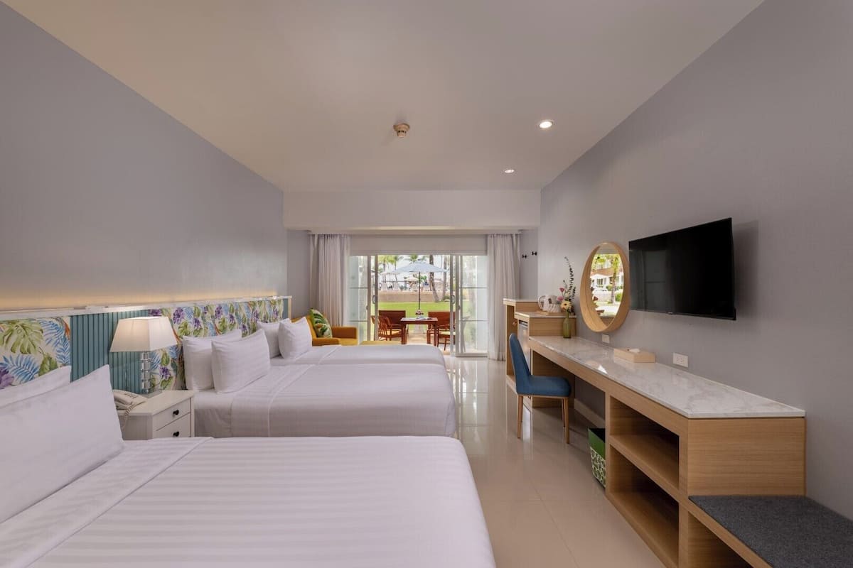A hotel room with two beds, a desk with a TV, and a view of the outdoor area.
