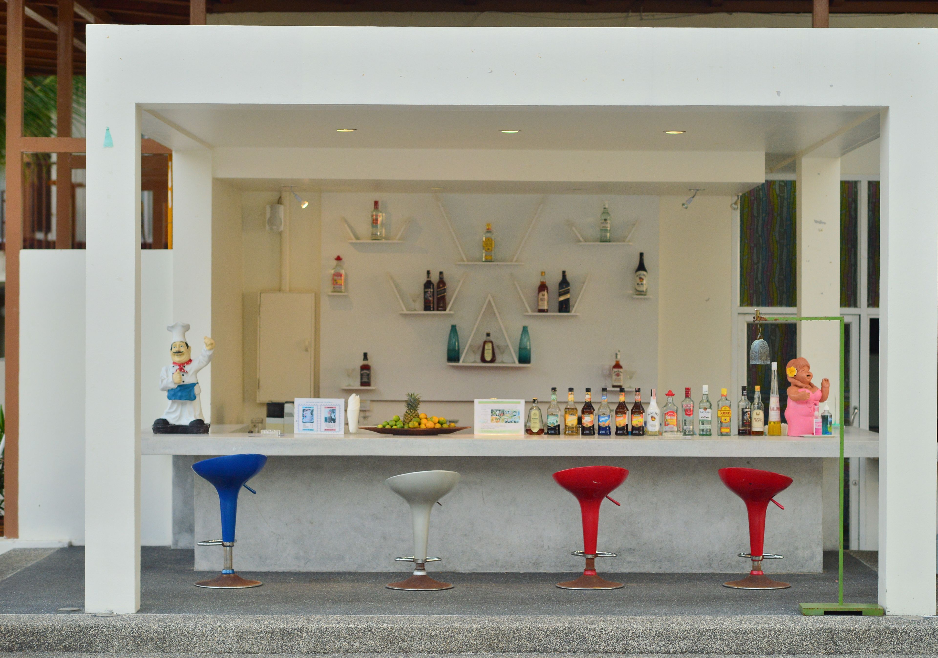 Un área de bar con mostrador, estantes con botellas y tres taburetes.