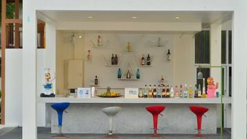 Un área de bar con mostrador, estantes con botellas y tres taburetes.
