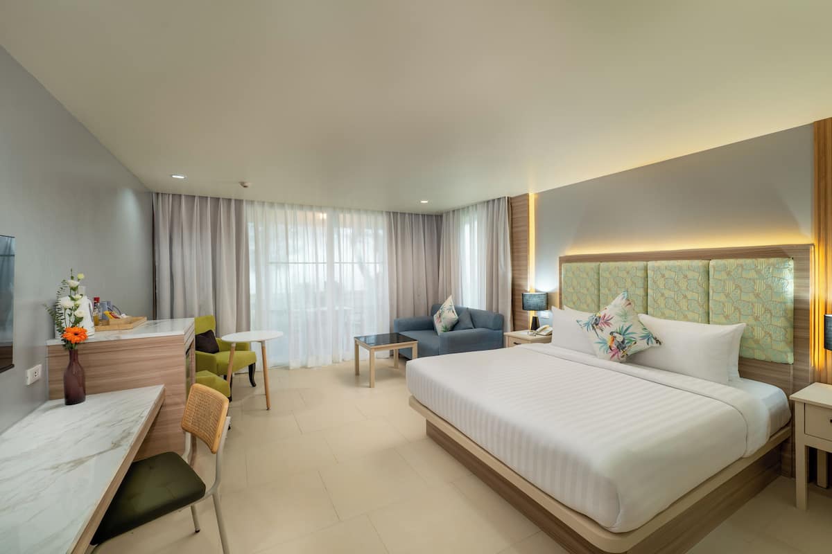 A hotel room with a bed, a desk, a chair, a small table, and a sofa.