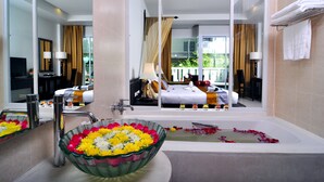 Een hotelbadkamer met een grote glazen schaal vol bloemen, een badkuip en een spiegel die de ruimte weerspiegelt.