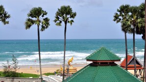 Vista de playa con palmeras, un pabellón y un edificio con techo verde.