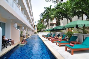 A swimming pool with lounge chairs and umbrellas, surrounded by buildings and palm trees. - Baan Karonburi Resort (Karon)