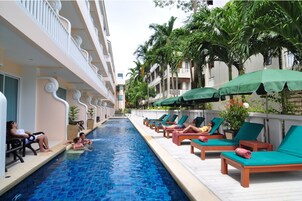 Una piscina con sillas de descanso y sombrillas, rodeada de edificios y palmeras.