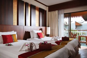 A hotel room with two beds, a balcony with a wooden railing, and a view of a building with a sloped roof.