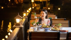 Comedor con mesas y sillas, iluminado por faroles, y una persona comiendo.