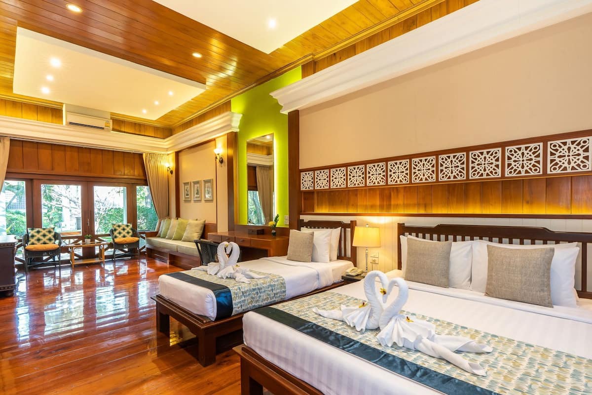 Una habitación de hotel con dos camas, piso de madera, un ventanal grande y un techo decorativo.
