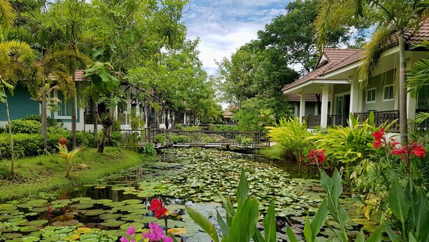 Un jardín tranquilo con un estanque, abundante vegetación y arquitectura tradicional.