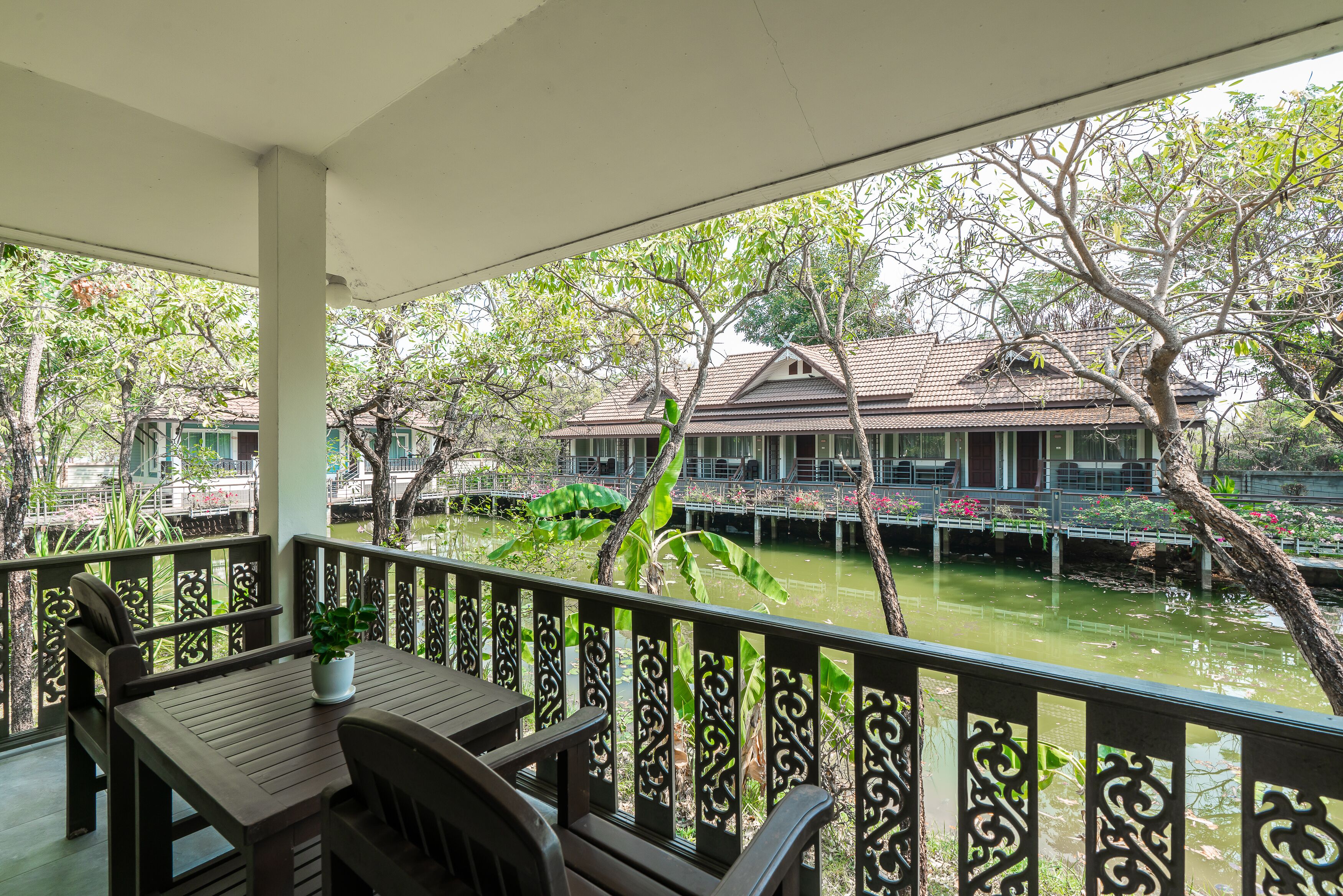 A covered balcony with a table and chairs, overlooking a river with a house across the water.