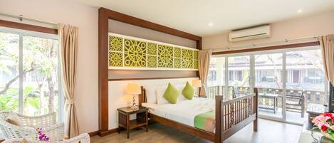 Habitación de hotel con cama, una silla, una mesa con flores y un balcón con mobiliario exterior.