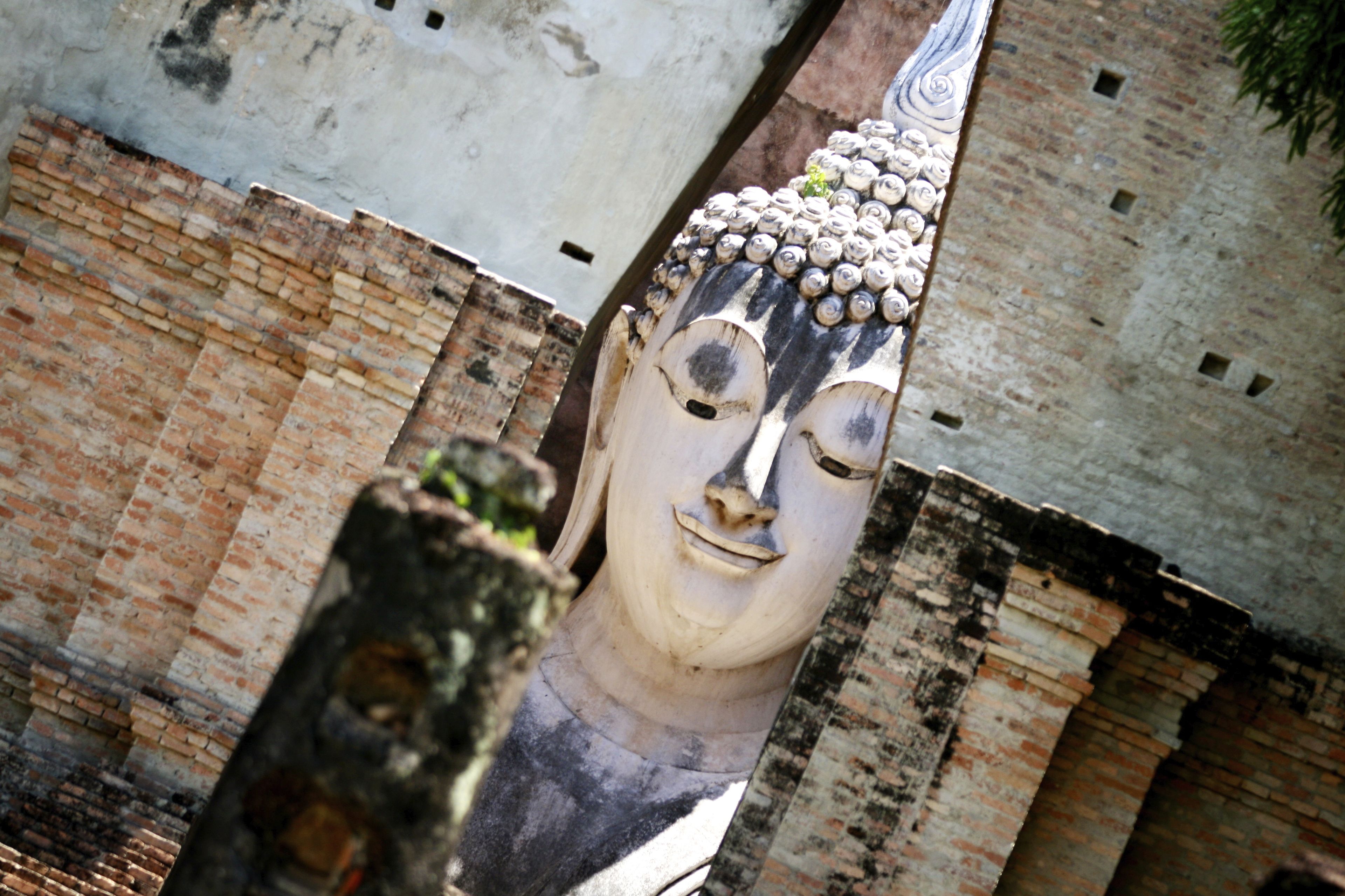 A large, weathered Buddha statue with a detailed headdress, set against a backdrop of aged brick walls.