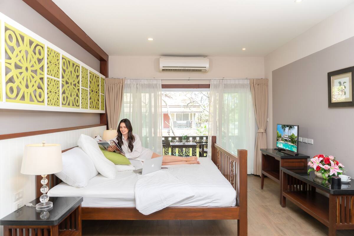 Una habitación de hotel con cama, escritorio con laptop, televisor y ventana con cortinas.