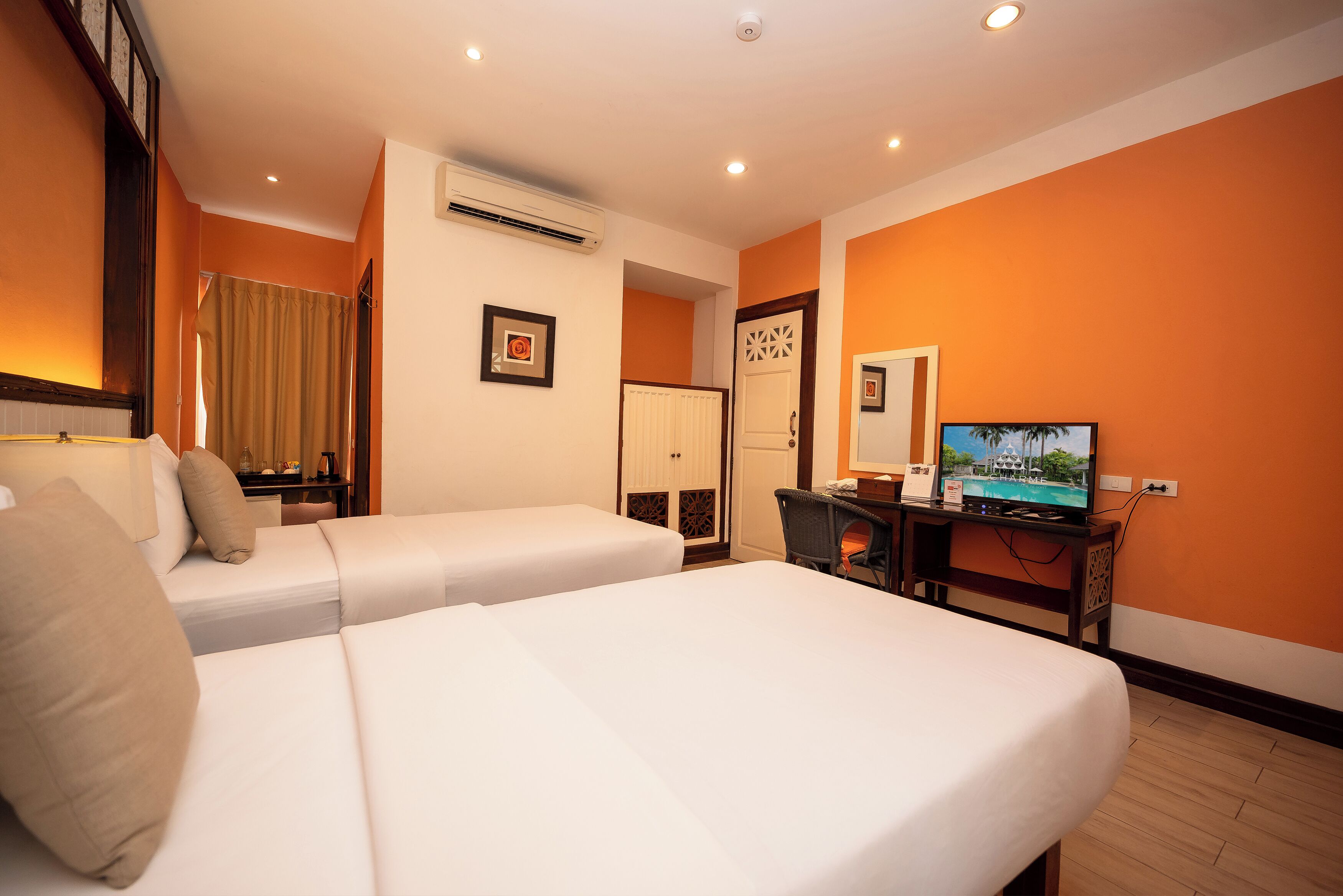 Habitación de hotel con dos camas, un escritorio con televisor, aire acondicionado y una puerta con panel decorativo.