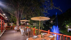 Un espacio de comedor al aire libre con mesas y sillas, rodeado por una terraza de madera y una barandilla roja.