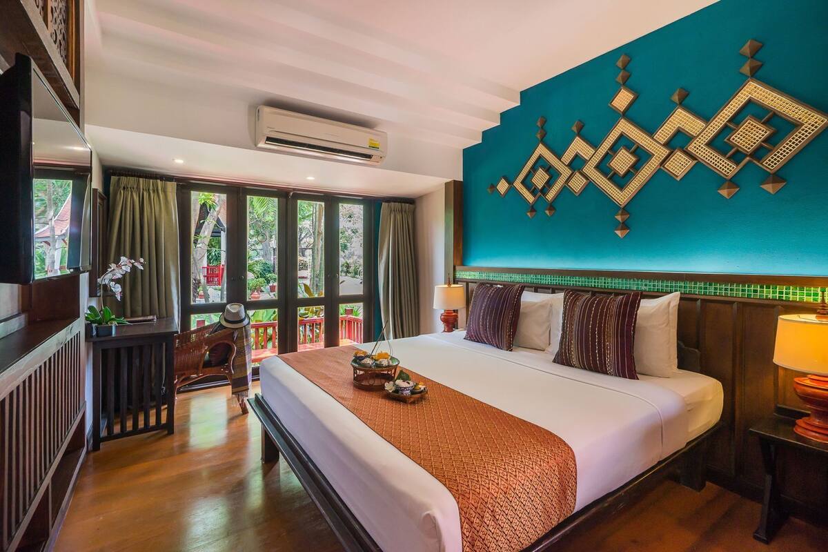 A hotel room with a large bed, a view through the windows, and a decorative wall piece.