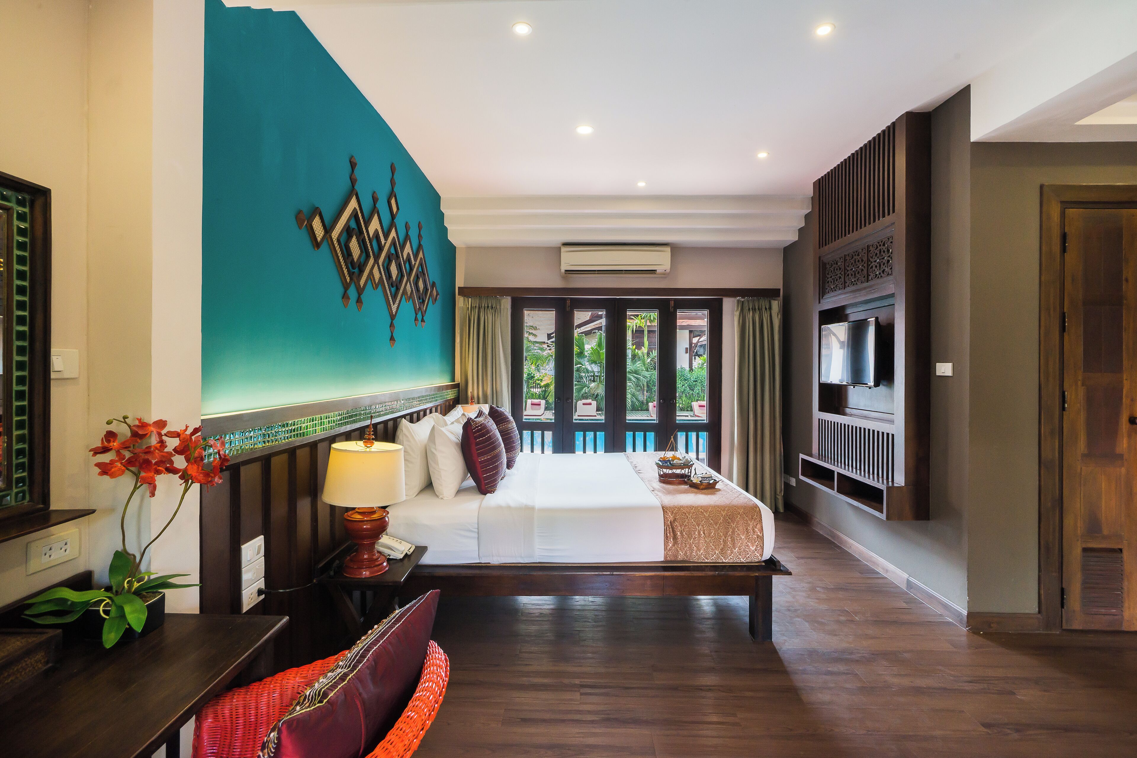 A spacious hotel room with a large bed, a TV mounted on the wall, and a view of the outdoors through the windows.
