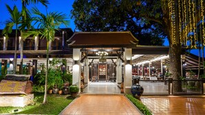 Entrada de hotel con un paseo techado, palmeras y un letrero.
