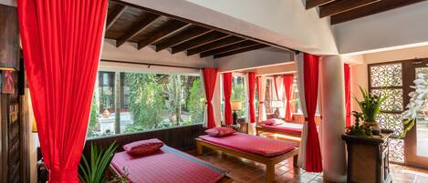 Un cuarto de spa con dos camillas de masaje, cortinas rojas y vistas al jardín.