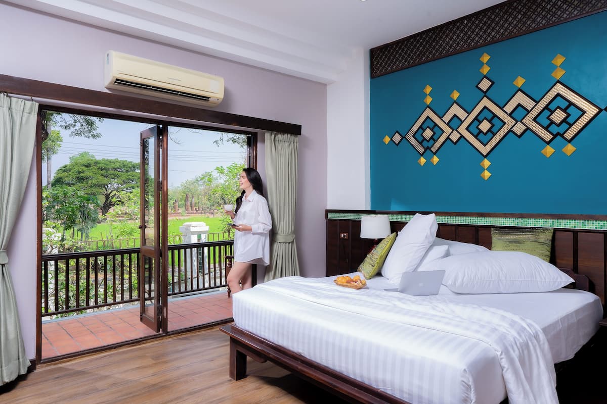 A hotel room with a bed, a laptop, and a view of a garden through a sliding door.