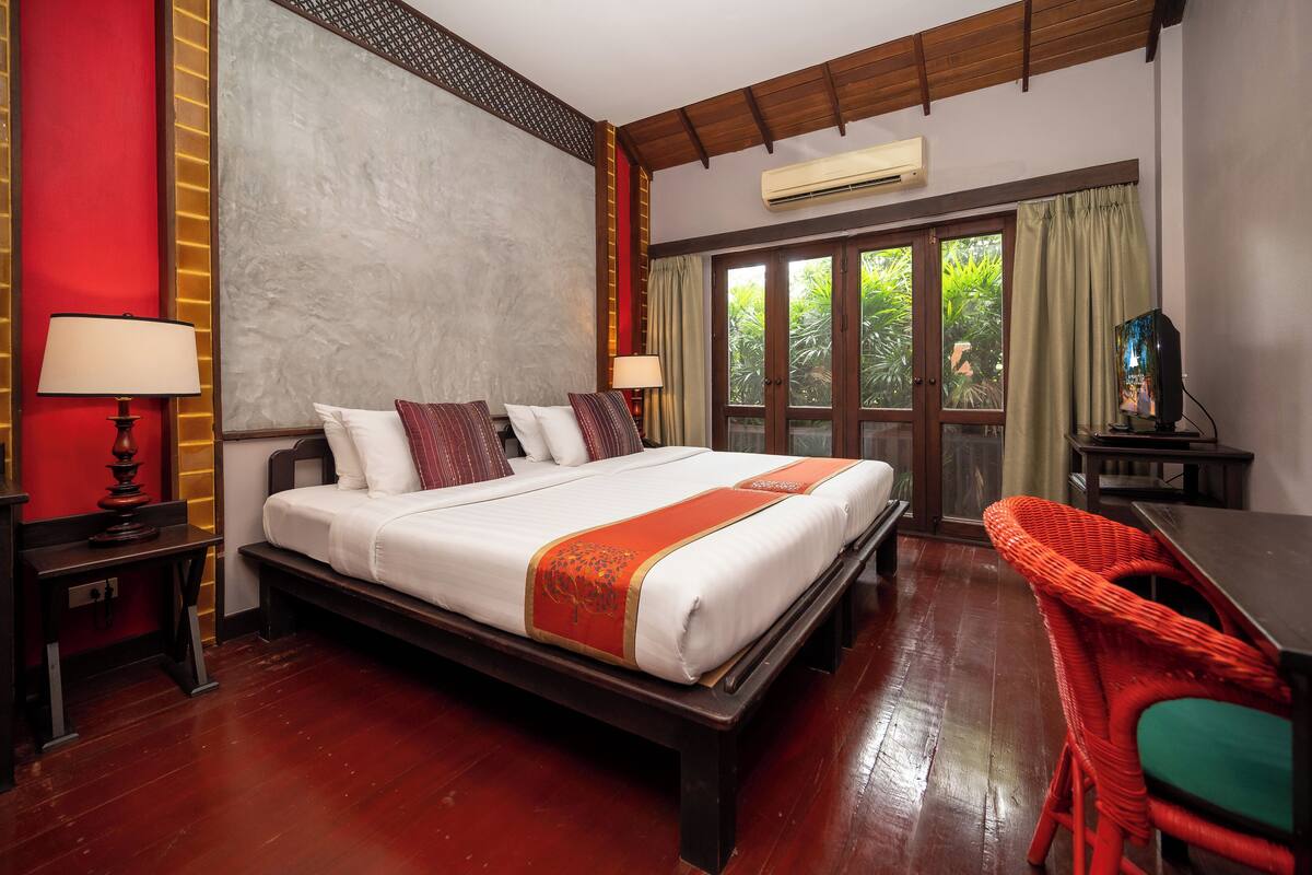 A hotel room with a large bed, a wooden floor, a TV, and a balcony with curtains.